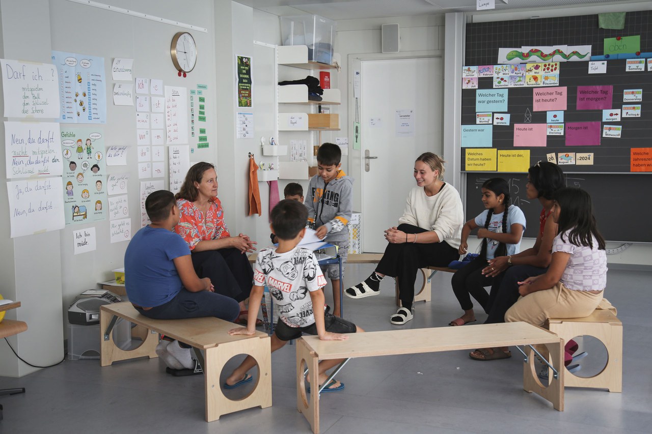 Schülerinnen und Schüler samt Lehrpersonen sitzen im Kreis